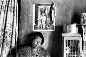 Мечты? Реальность или желаемое? Жена работника фермы с своем доме рядом с фотографией “настоящей американской” семьи на стене. Южная Африка, Оудсхорн, 2003